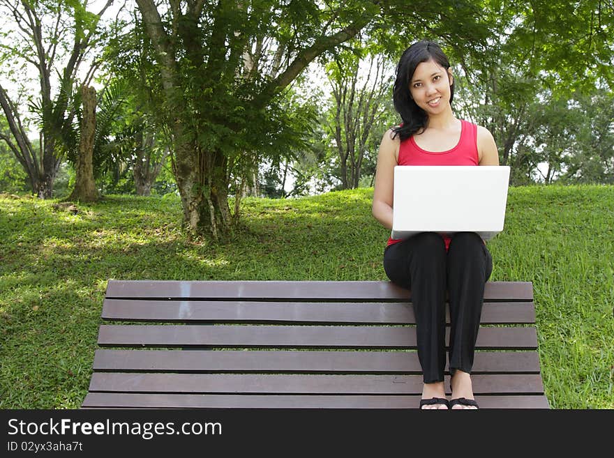 An Asian woman with a laptop sitting on a bench. An Asian woman with a laptop sitting on a bench