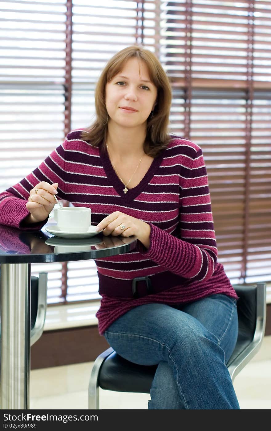 The girl drinks coffee behind a table in cafe