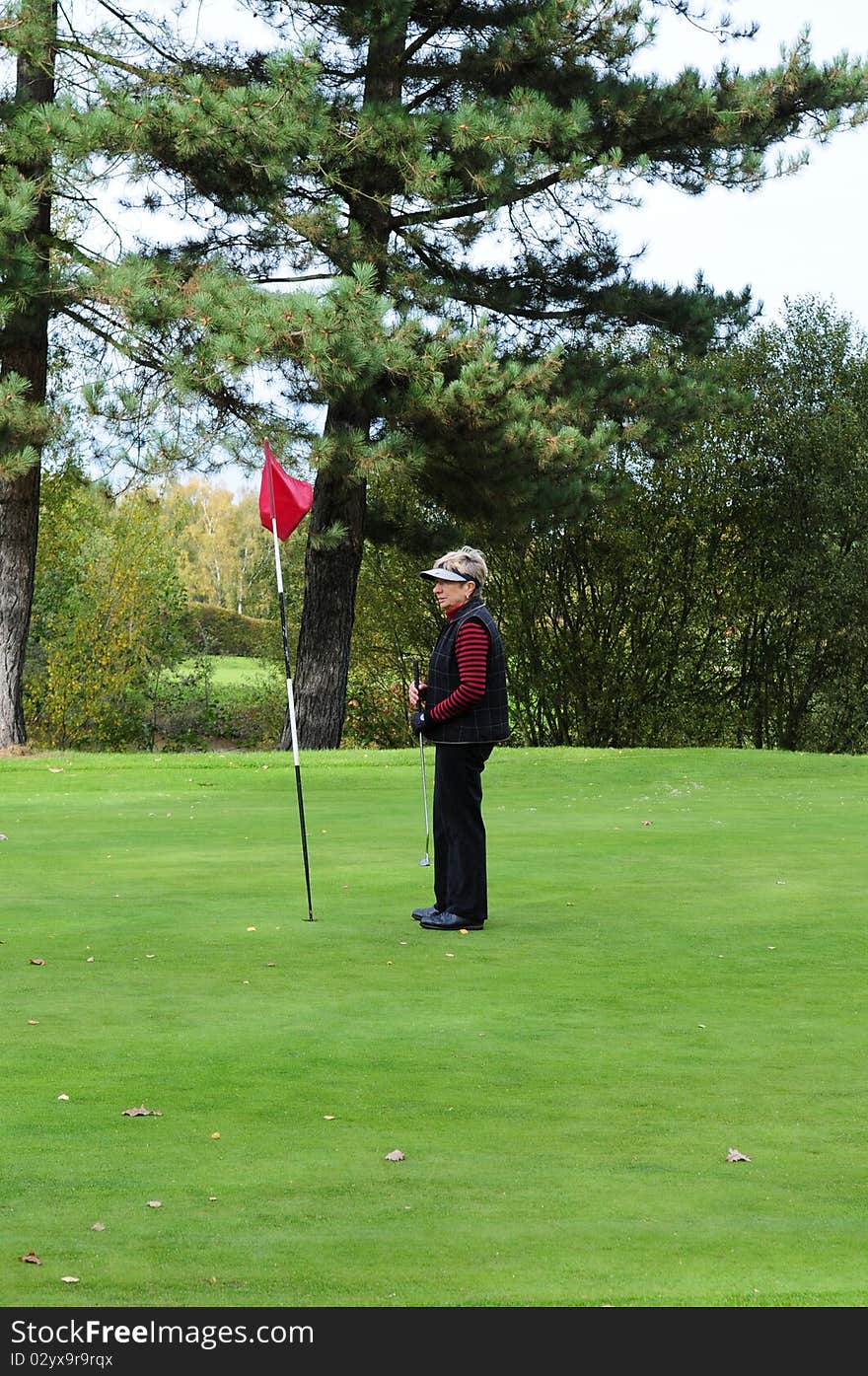 Female golfer standing on the green next to the putting flag. Female golfer standing on the green next to the putting flag