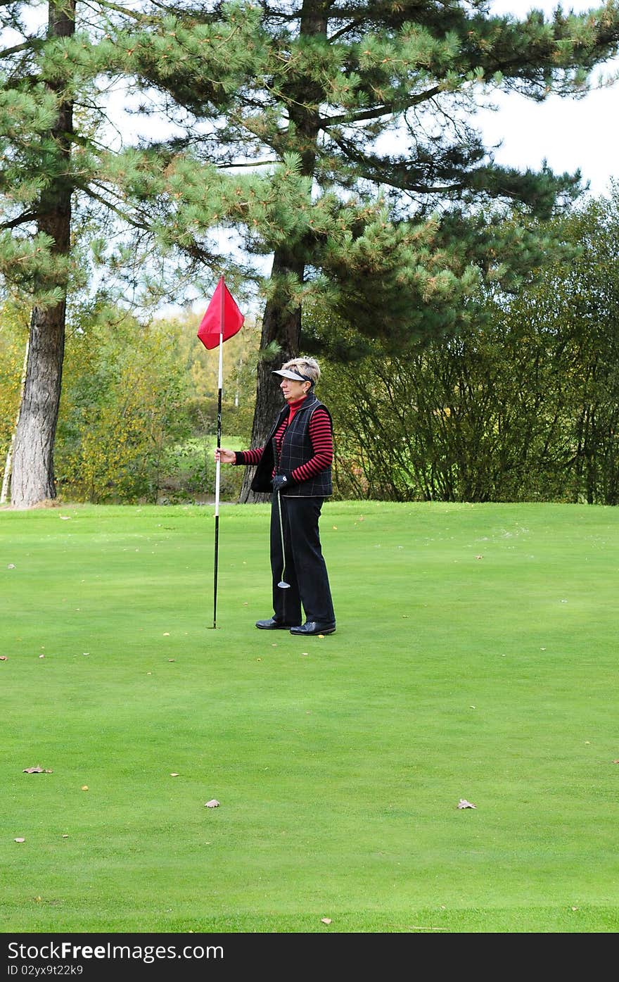 Female golfer standing on the green holding the putting flag. Female golfer standing on the green holding the putting flag