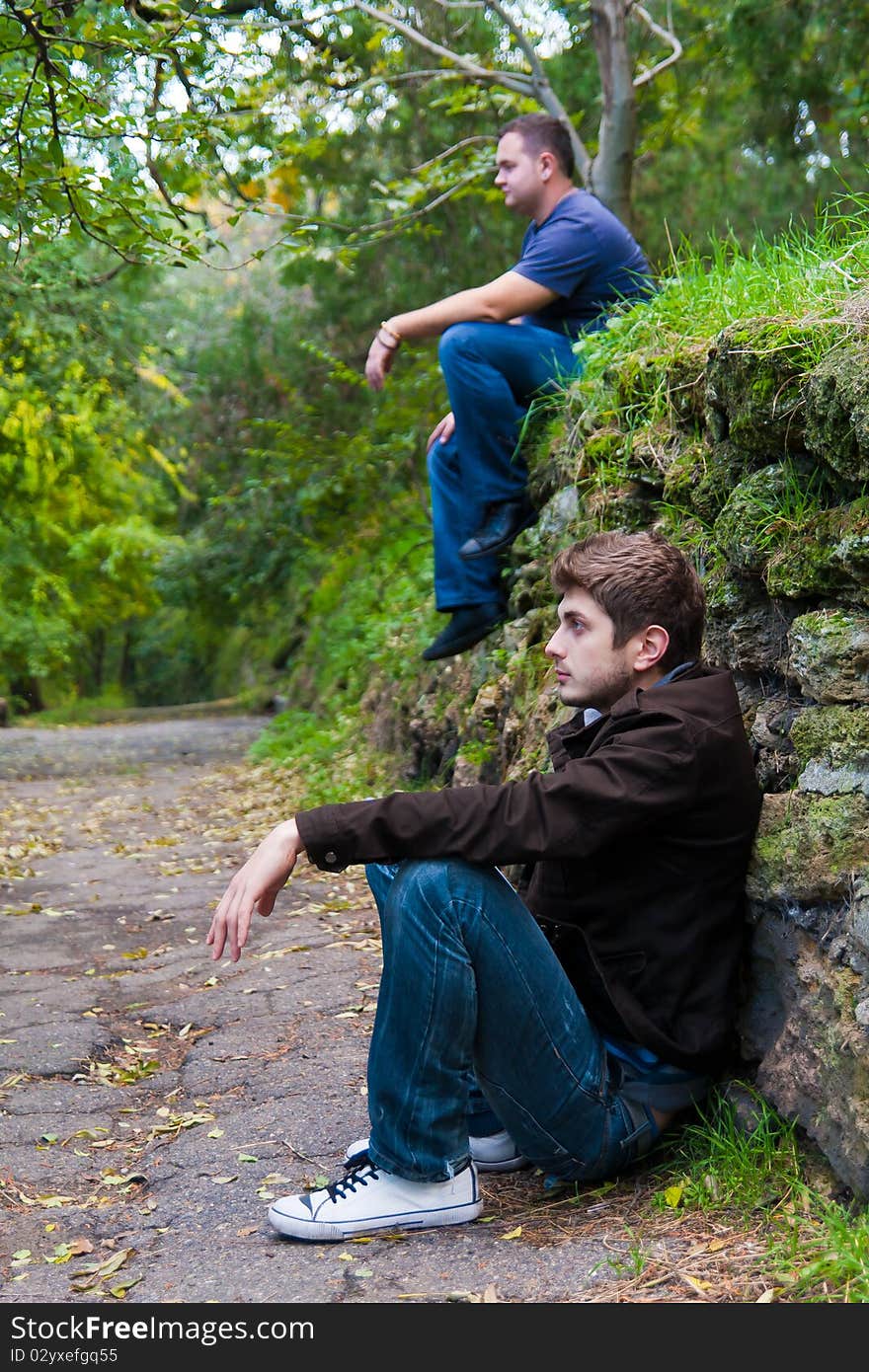 Two man in the park in the same pose like twins. Two man in the park in the same pose like twins