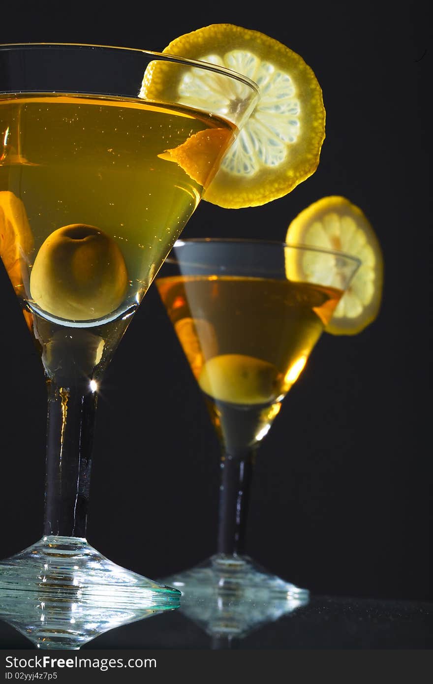 Two bocals of martini with olive and lemon on black background. Two bocals of martini with olive and lemon on black background