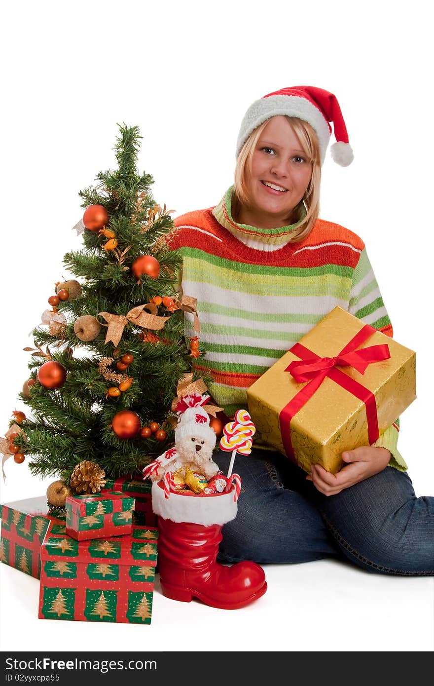 Young woman with santa hat sitting beside a christmas tree with christmas gifts - isolated. Young woman with santa hat sitting beside a christmas tree with christmas gifts - isolated