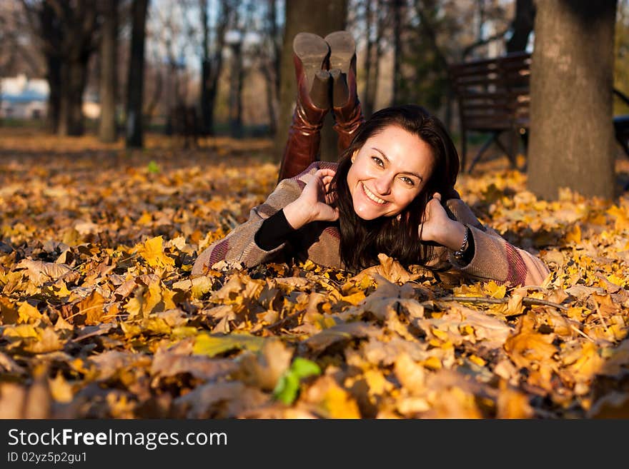 Beautiful young woman smiling lying down in autumn leaves in park. Beautiful young woman smiling lying down in autumn leaves in park