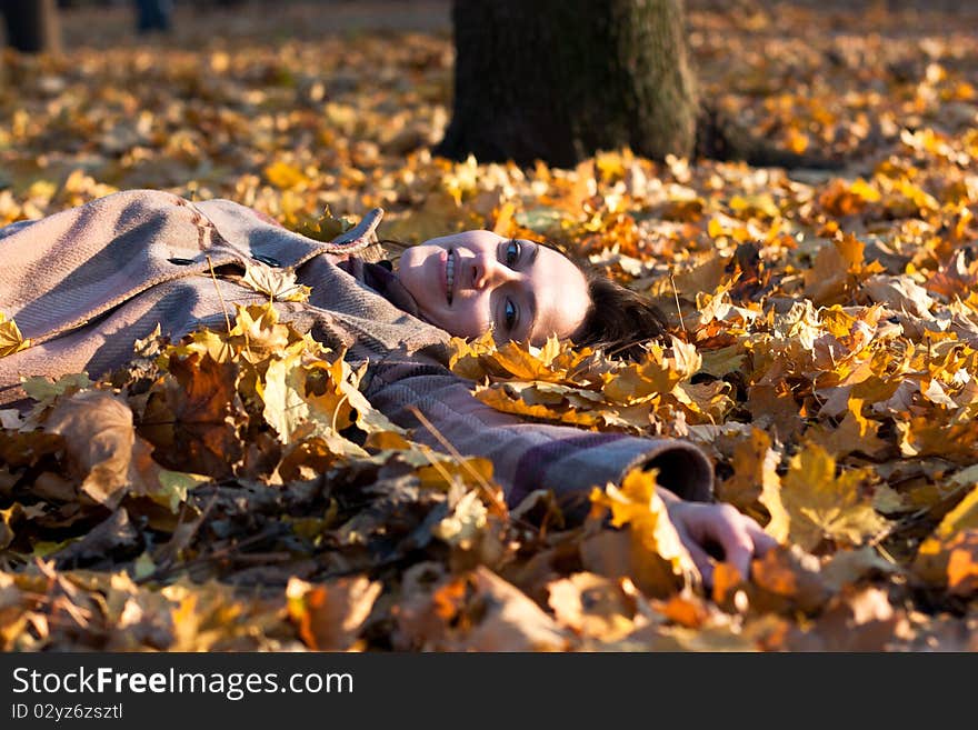 Beautiful young woman lying down in autumn leaves in park. Beautiful young woman lying down in autumn leaves in park