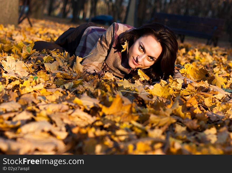 Beautiful young woman lying down in autumn leaves in park. Beautiful young woman lying down in autumn leaves in park