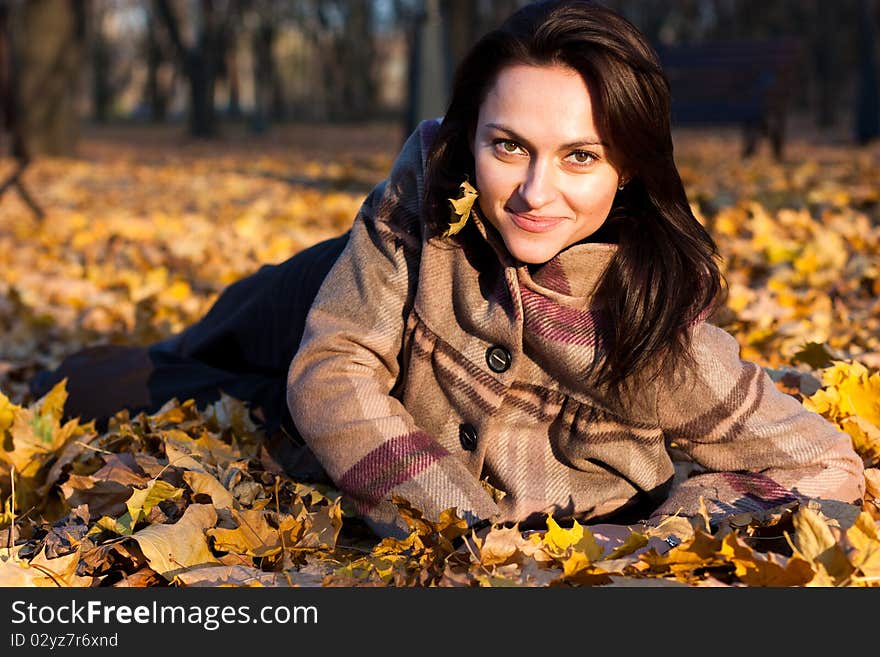 Beautiful young woman lying down in autumn leaves in park. Beautiful young woman lying down in autumn leaves in park