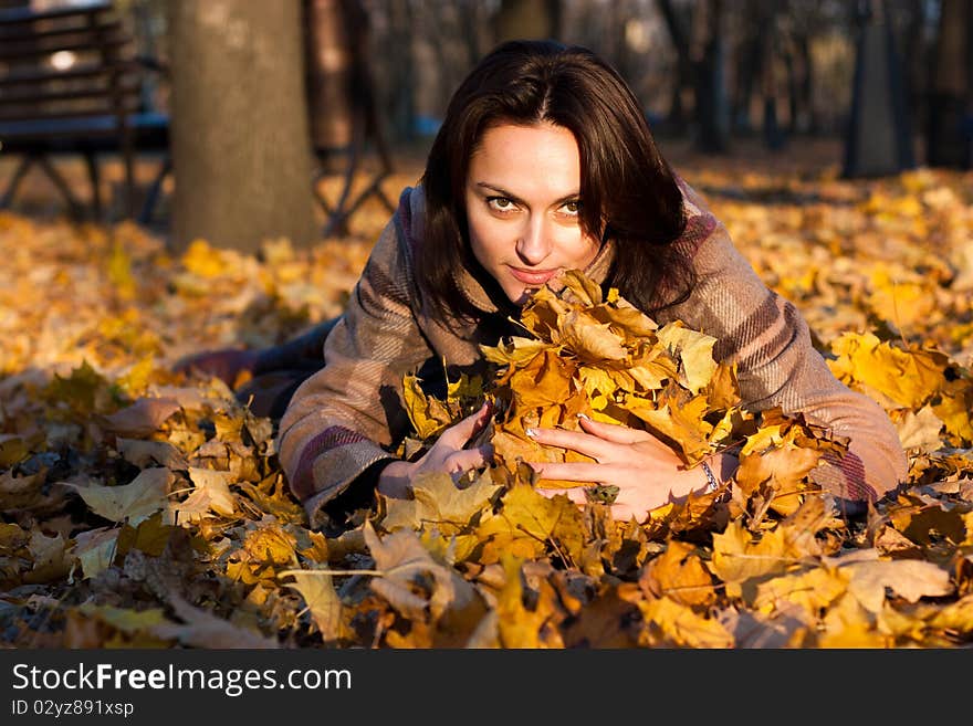 Beautiful young woman lying down in autumn leaves in park. Beautiful young woman lying down in autumn leaves in park