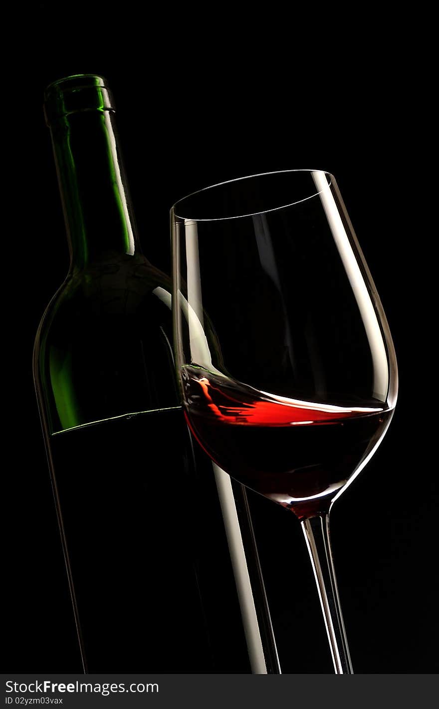 Glass of red wine with a bottle and black background