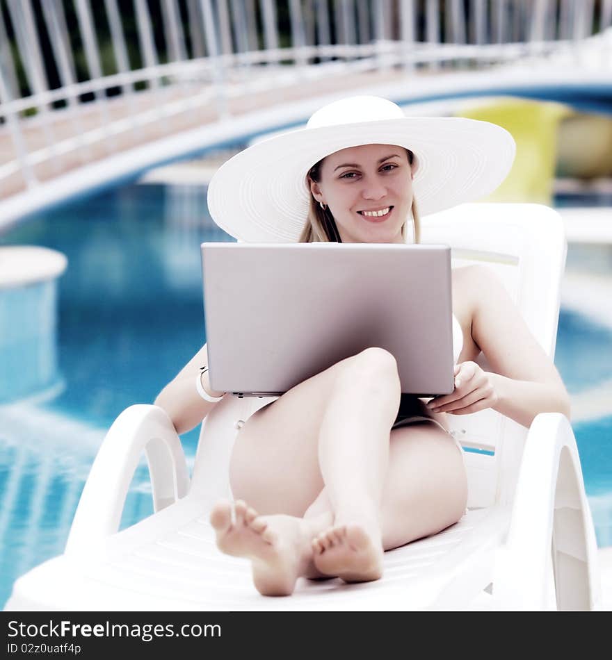 Young women relaxing near waterpool with laptop.