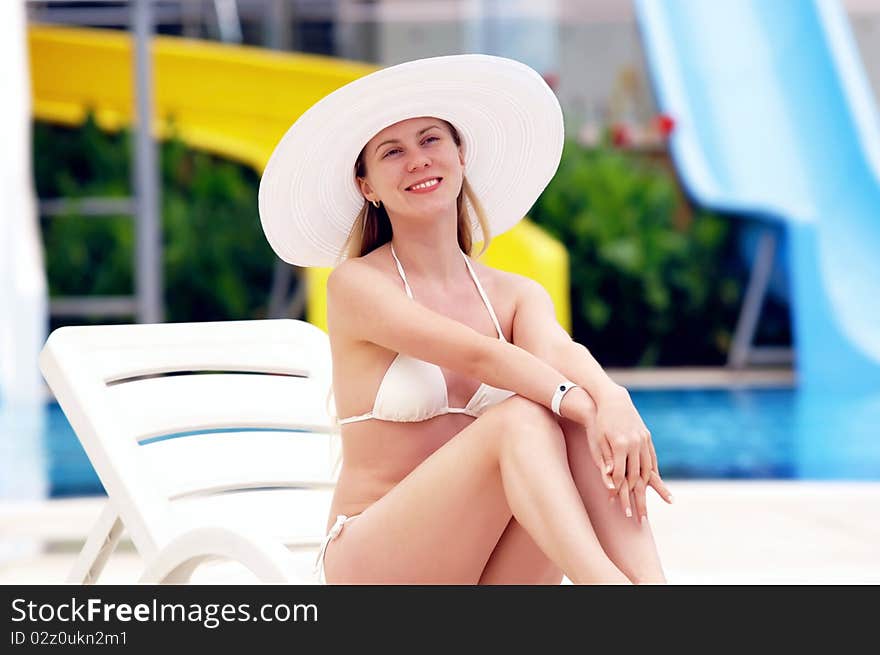 Young women in white bikini and white hat relaxing near waterpool