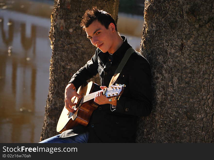 Happy man playing guitar on the middle of nature, under a tree. Happy man playing guitar on the middle of nature, under a tree