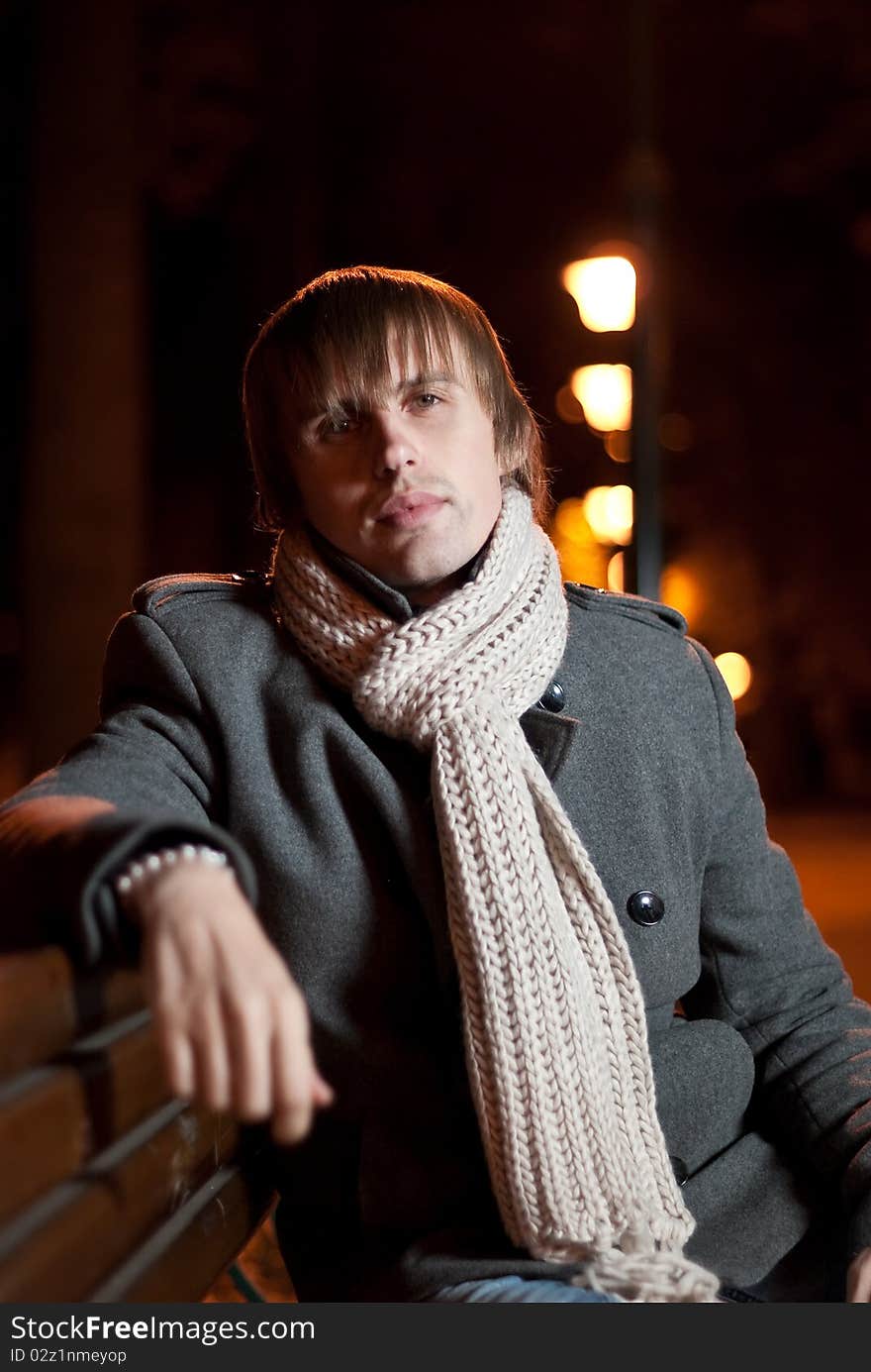 Young man in coat sitting at night park alley. Young man in coat sitting at night park alley