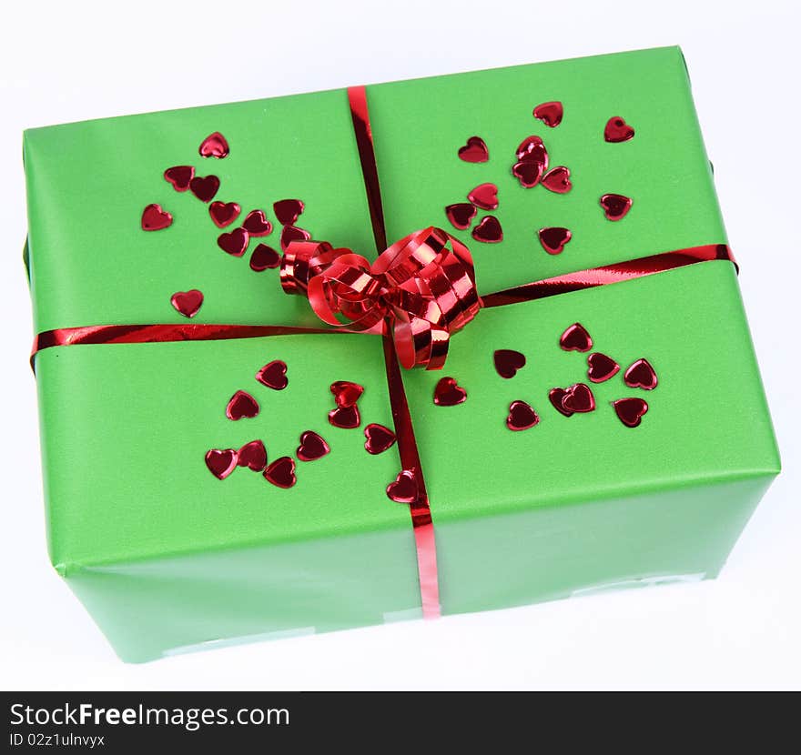 Gift in green wrapping with a red bow decorated with heart shaped confetti