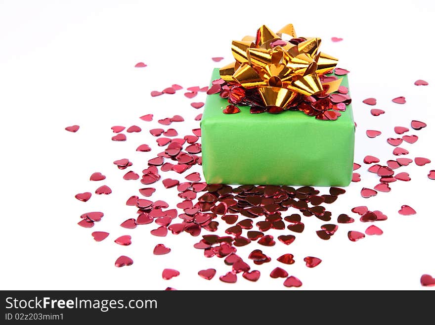 Gift in green wrapping with a golden bow decorated with heart shaped confetti. Gift in green wrapping with a golden bow decorated with heart shaped confetti