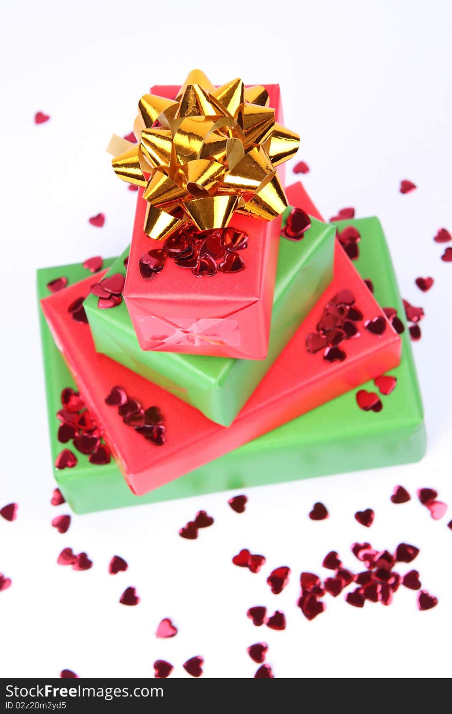 Gifts in green and red wrapping with a golden bow decorated with heart shaped confetti. Gifts in green and red wrapping with a golden bow decorated with heart shaped confetti