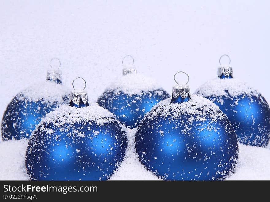 Blue matt christmas balls on snow and with snow falling on white background