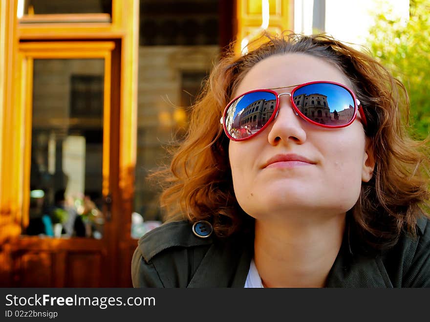 Portait of a youg woman smiling, with red sunglasses reflecting a nearby building. Portait of a youg woman smiling, with red sunglasses reflecting a nearby building