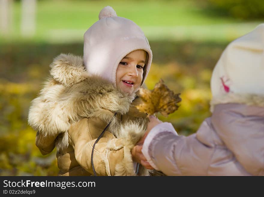 Two little girls playing with autumn leave in the park