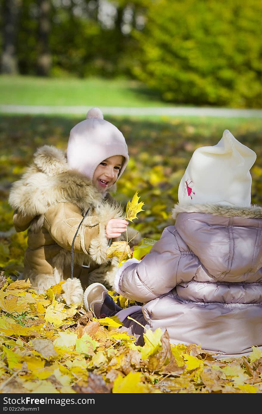 Two little girls playing with autumn leave in the park