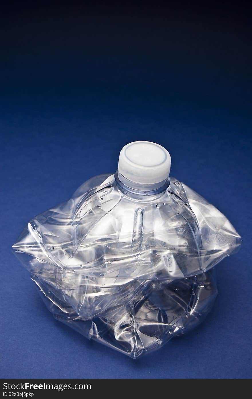 Plastic bottle crushed to be thrown in the garbage in front of a blue and black background