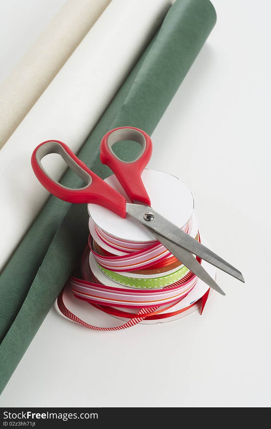 Red handled scissors on top of a stack of red and green ribbon with gift wrapping paper. Red handled scissors on top of a stack of red and green ribbon with gift wrapping paper