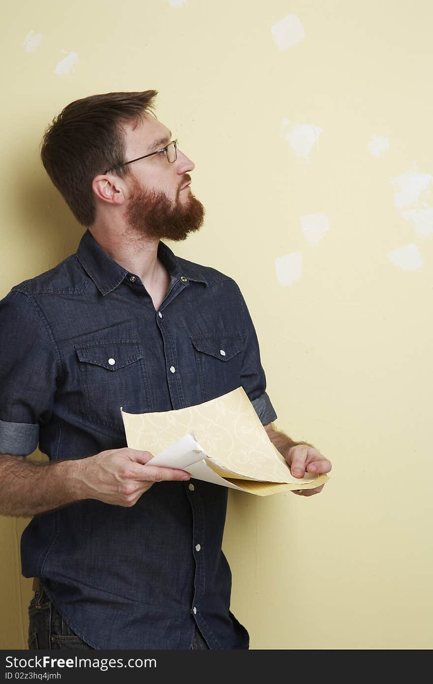 Man with beard and denim shirt leans against a wall holding other samples in his hand. Man with beard and denim shirt leans against a wall holding other samples in his hand