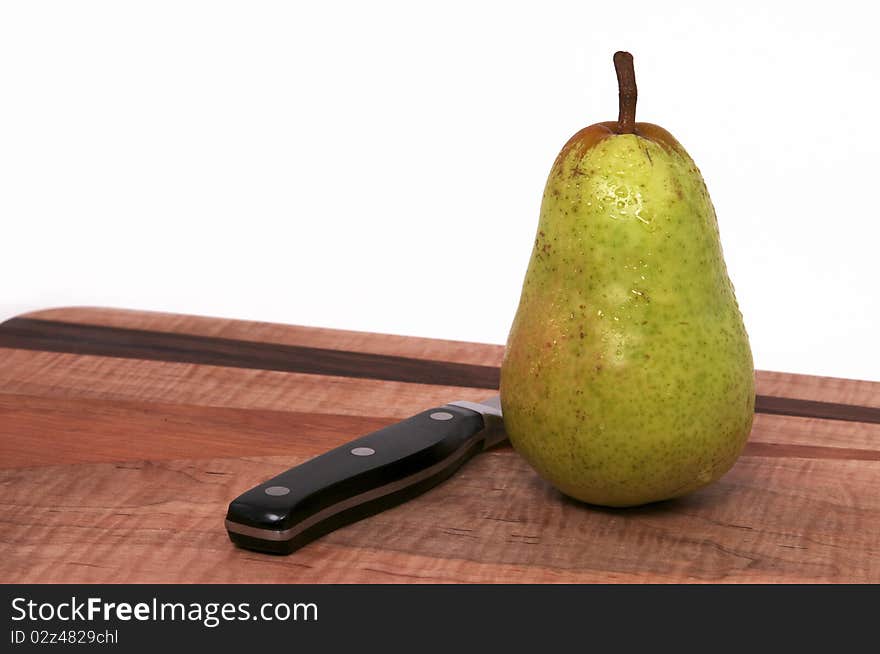 A Single Pear on a Wood Cutting Board with Black Knife Isolated against a White Background