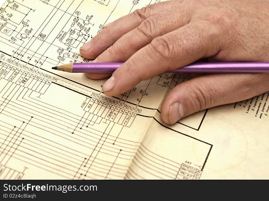 Human hand with pencil on electroscheme in operation