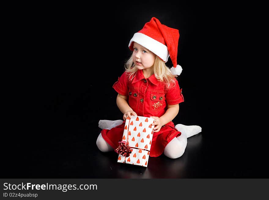 Surprised girl in red dress and santa cap with gift box. Isolated on black. Surprised girl in red dress and santa cap with gift box. Isolated on black