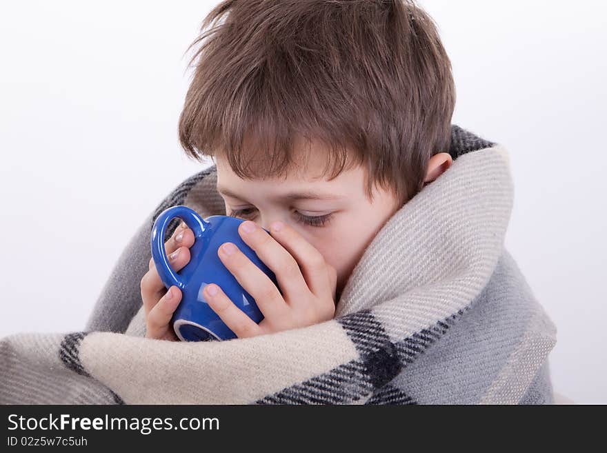 The boy covered by a checkered plaid, drinks from a dark blue cup