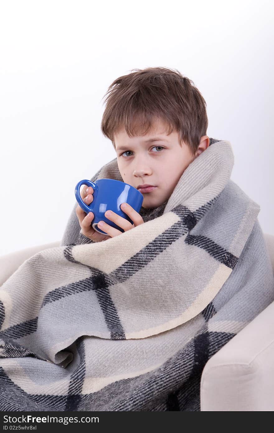 The boy covered by a checkered plaid, drinks from a dark blue cup