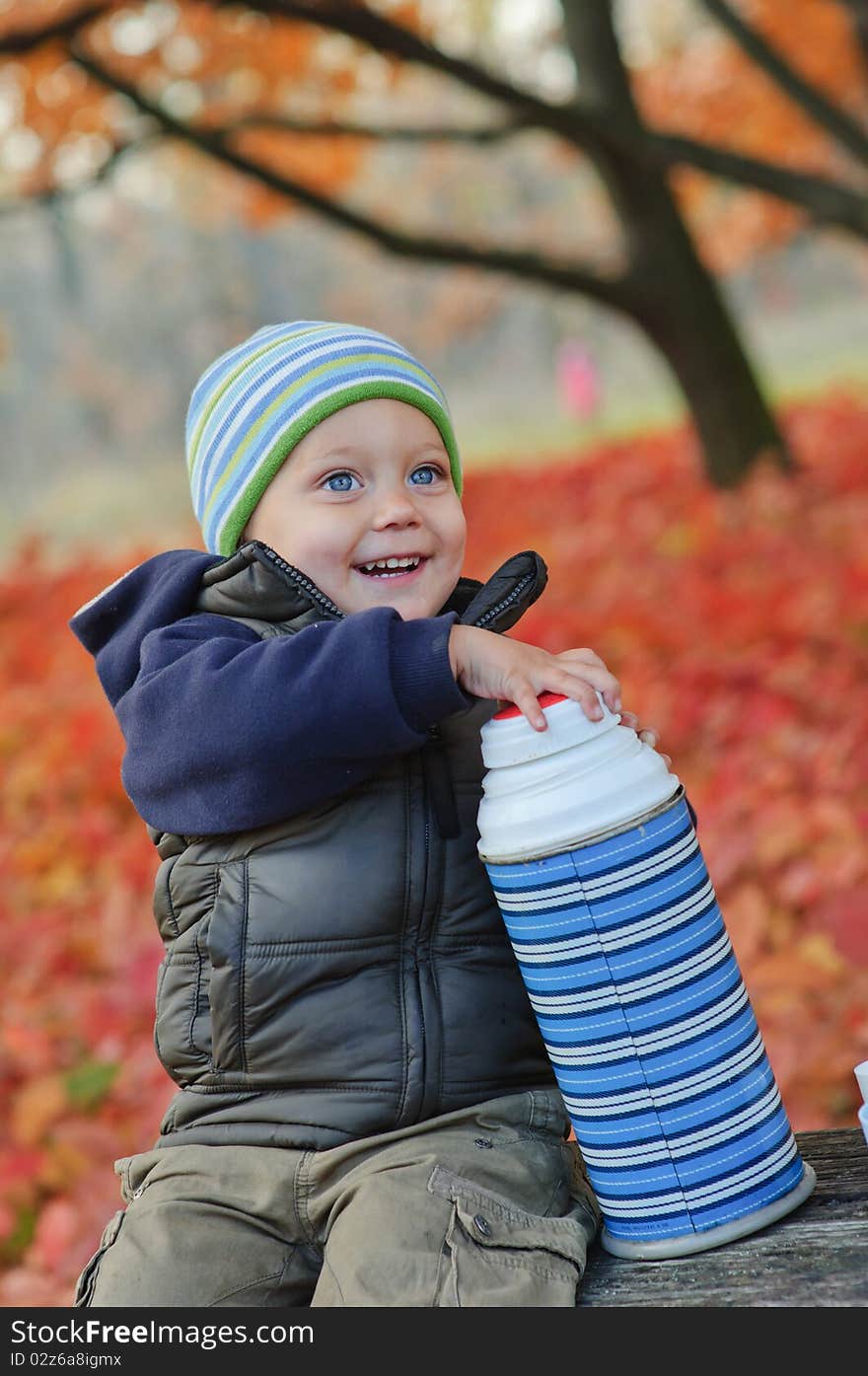 Little cute boy drinks tea from a thermos in the autumn park