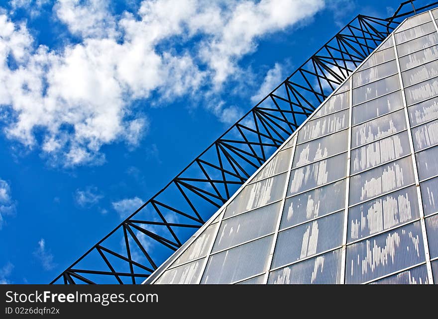 Glass wall of a greenhouse (conservatory) against blue sky and clouds