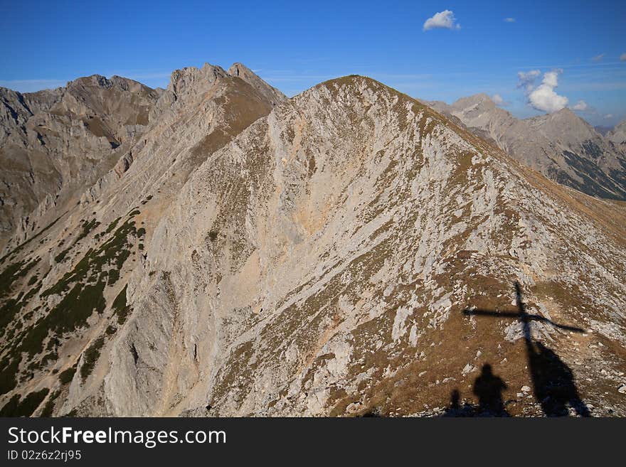 Hiking in Austrian mountains in autumn, blue sky, summit cross as a shadow. Hiking in Austrian mountains in autumn, blue sky, summit cross as a shadow