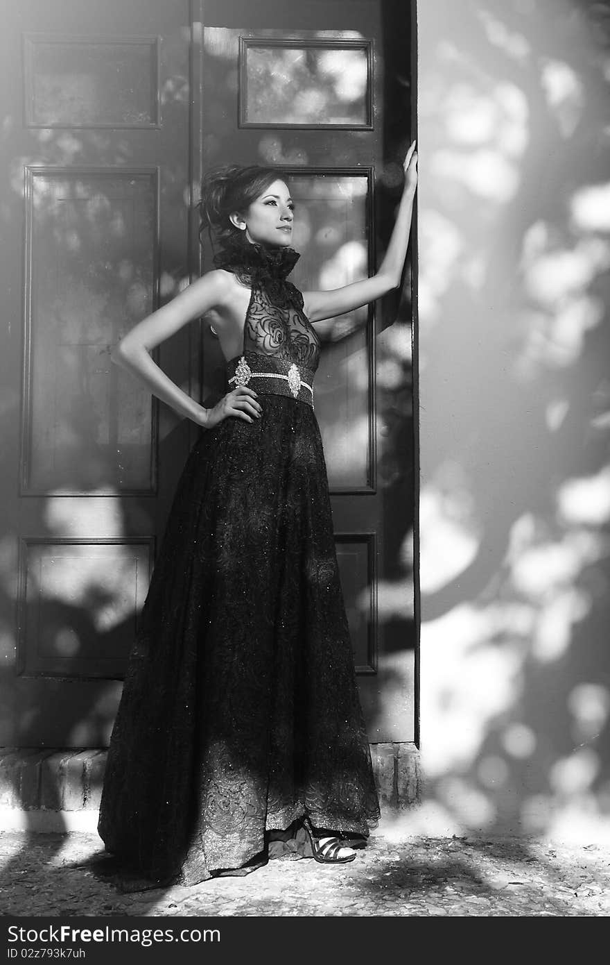 Black and white photo of a Model pose in front of a door. In the wall can see the shadows of a tree. Black and white photo of a Model pose in front of a door. In the wall can see the shadows of a tree.