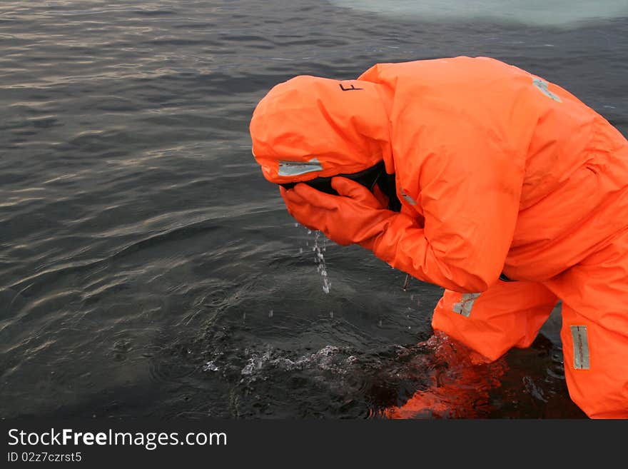 Human being in the water in a red rescue suit. The human being wash his face with cold water. Maybe his eyes are burning because of rays, heat or fire. Human being in the water in a red rescue suit. The human being wash his face with cold water. Maybe his eyes are burning because of rays, heat or fire.