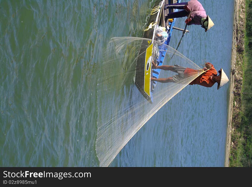 Couple fishing with a net into the boat. The woman stabilizes the boat with his oar while the man goes back in net. Couple fishing with a net into the boat. The woman stabilizes the boat with his oar while the man goes back in net.