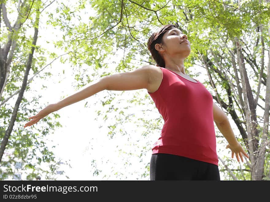 An Asian woman spreading her arms at a park enjoying the peaceful surrounding. An Asian woman spreading her arms at a park enjoying the peaceful surrounding