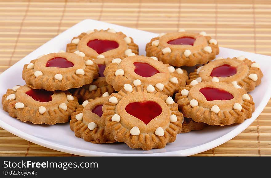 Cookies with a stuffing from red fruit jelly in the form of heart lay on the white plate. Sweet valentine. Closeup. Cookies with a stuffing from red fruit jelly in the form of heart lay on the white plate. Sweet valentine. Closeup.