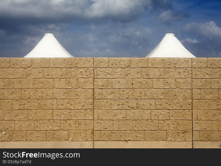 The tops of two white big umbrellas are behind a wall made of bricks. The tops of two white big umbrellas are behind a wall made of bricks