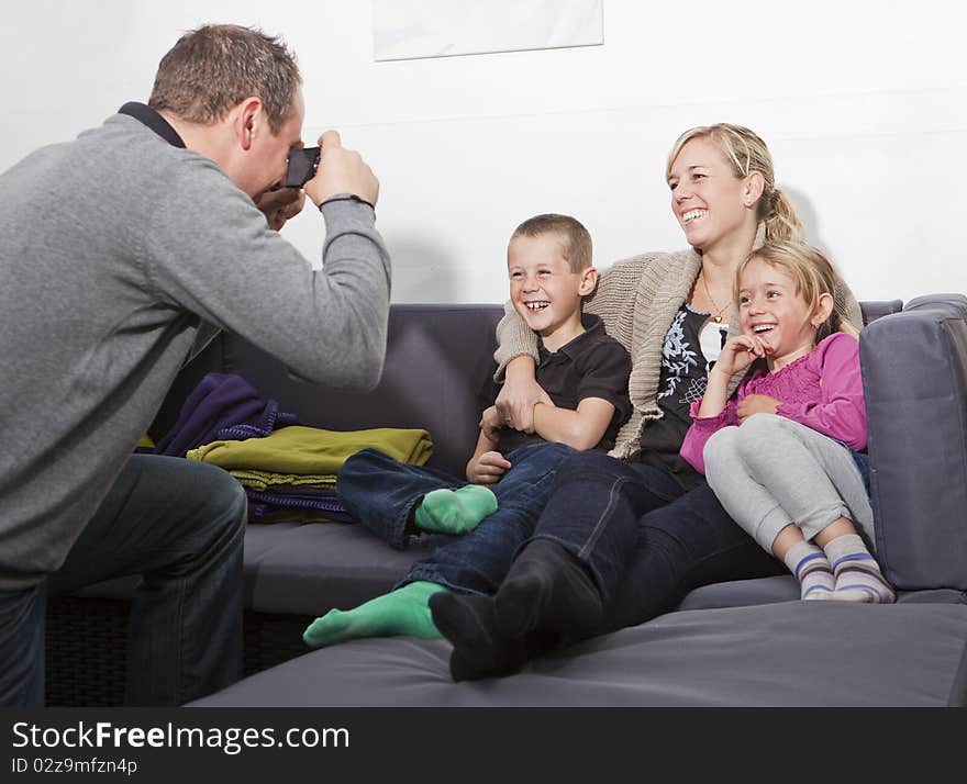 Father taking a photo of his family siting in the sofa