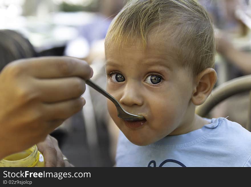 Beautiful baby boy is being feed with a spoon. Great detail on his blue eyes.