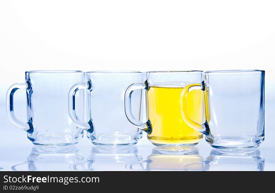 Four glass cups three of which are empty and one with a yellow tea