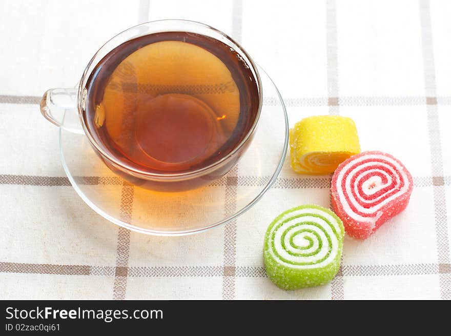 Colored jelly and mug with tea on checkered tablecloth