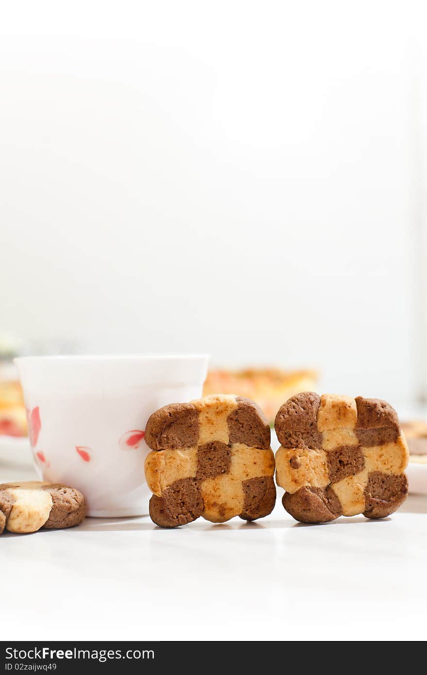 Assorted cookies in white plate and white mug of tea on white table. Assorted cookies in white plate and white mug of tea on white table