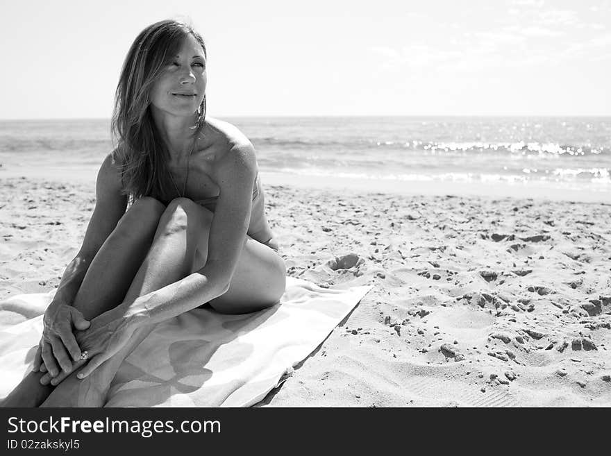 Female in 30's sitting on towel at beach looking away from camera.Black and White image. Female in 30's sitting on towel at beach looking away from camera.Black and White image