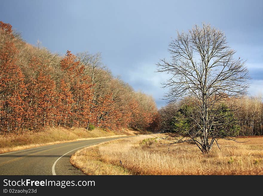 A curving road through a rural area of Michigan with the sun partially out and a stormy sky in the background.  Shot in the fall. A curving road through a rural area of Michigan with the sun partially out and a stormy sky in the background.  Shot in the fall.