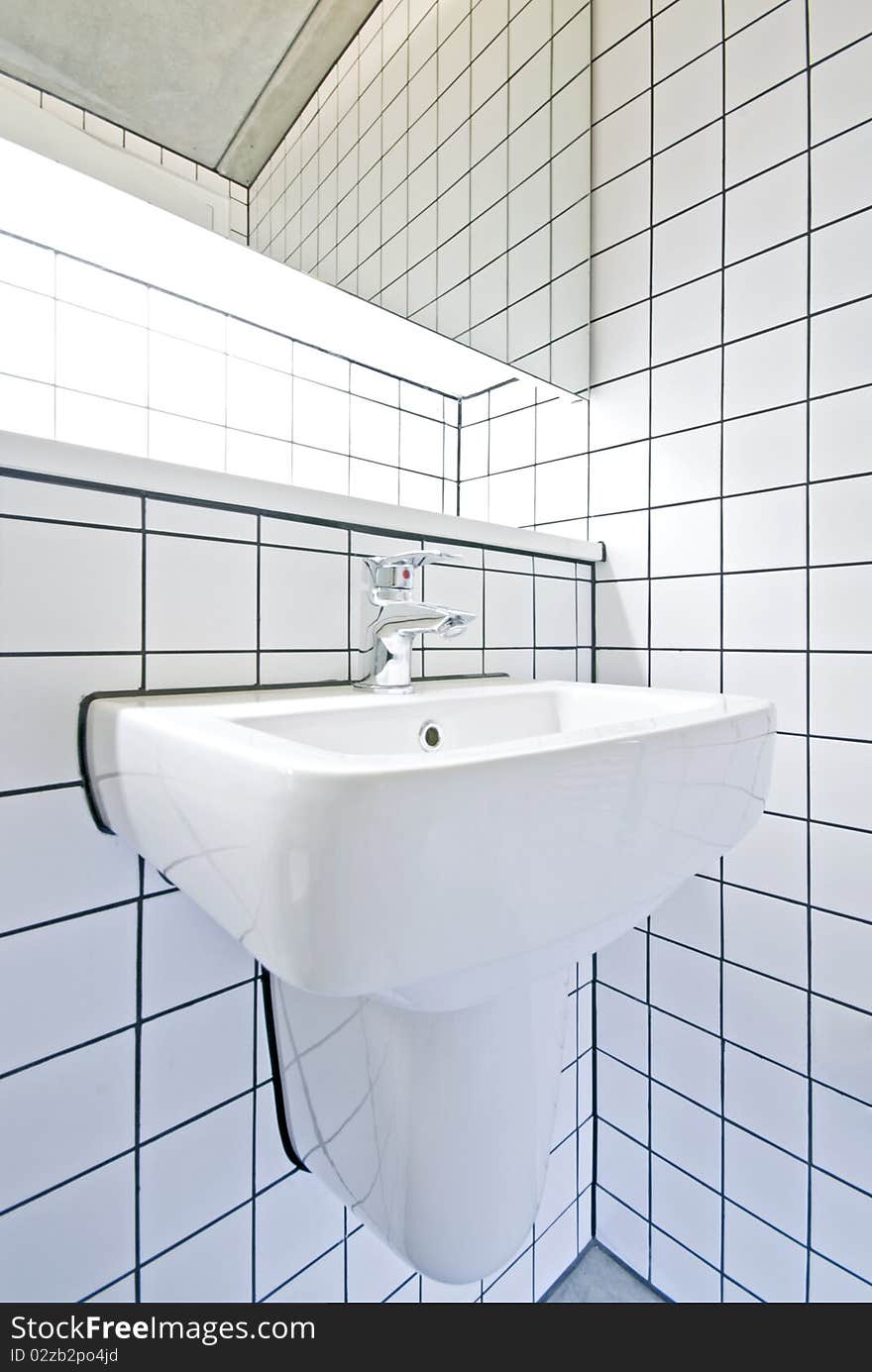 Detail of a contemporary bathroom with white ceramic hand was basin, large mirror and retro white tiled walls situated in a warehouse conversion building. Detail of a contemporary bathroom with white ceramic hand was basin, large mirror and retro white tiled walls situated in a warehouse conversion building