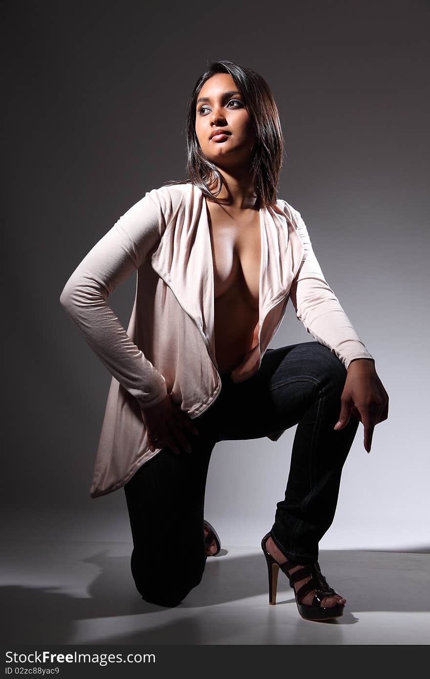 Beautiful and voluptuous young fashion model in a kneeling pose, head turned away. Wearing high heels, blue jeans and open front long sleeve shirt top. Beautiful and voluptuous young fashion model in a kneeling pose, head turned away. Wearing high heels, blue jeans and open front long sleeve shirt top.